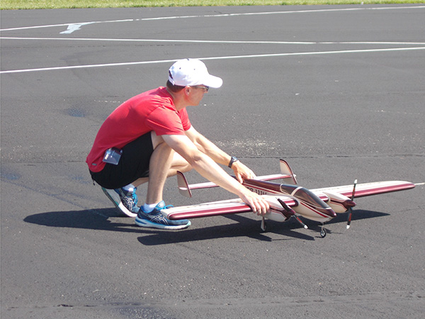 Man kneeling to launch a remote-controlled airplane on tarmac.