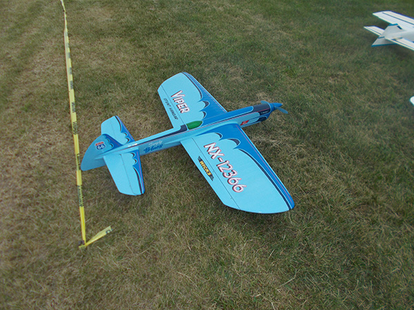 Blue model airplane on grass next to a yellow measuring tape.
