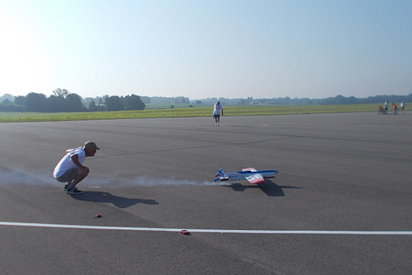 A person launching a model airplane on a sunny airfield.