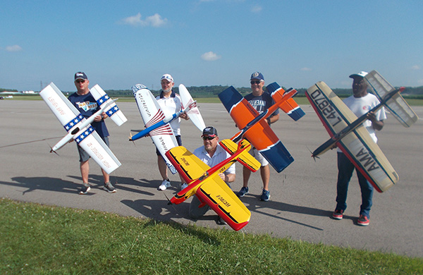 Five people posing with large model airplanes on a runway.
