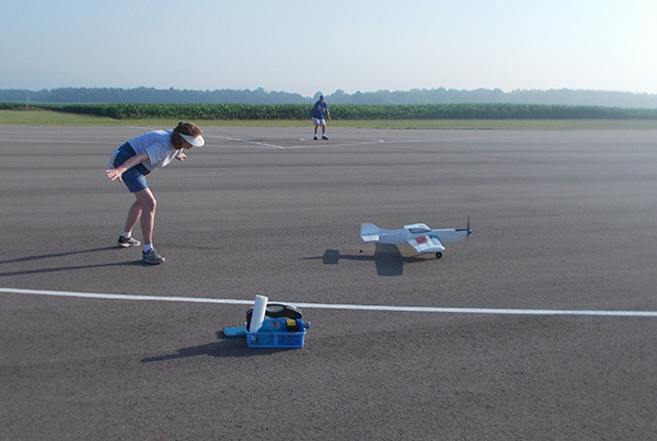 A person launching a small model airplane on a paved runway.