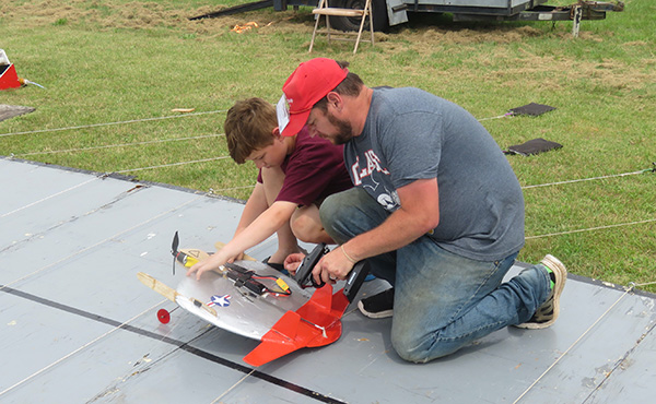 Father and son fixing a red and white model rocket outdoors.