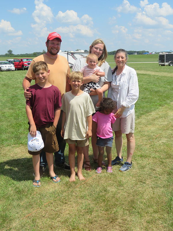 Family standing on a grassy field under a blue sky.