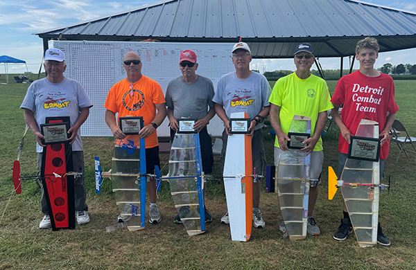 A group of six people holding small model airplanes outdoors.