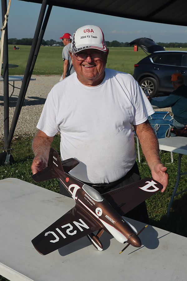 Man in white shirt holds a model airplane outdoors on a sunny day.