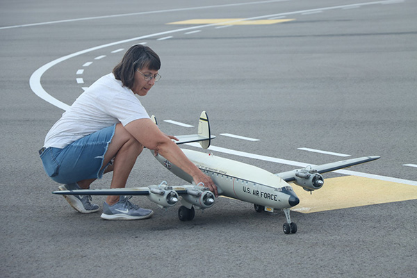 Woman adjusting a model airplane on a runway.