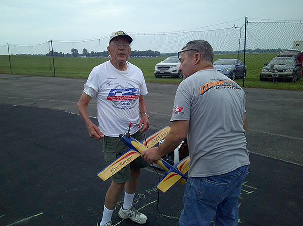 Two men outdoors with a model airplane on a tarmac.