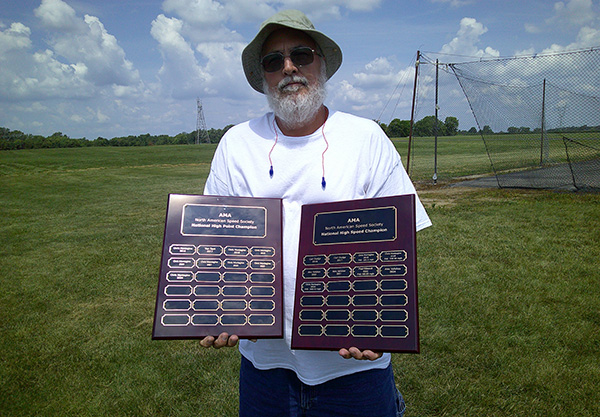 Man holding two award plaques outdoors on a sunny day.
