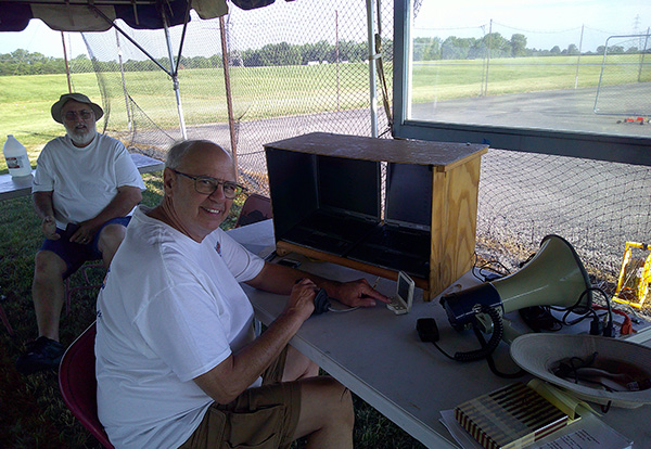 Two people sitting at a table with radio equipment outdoors.