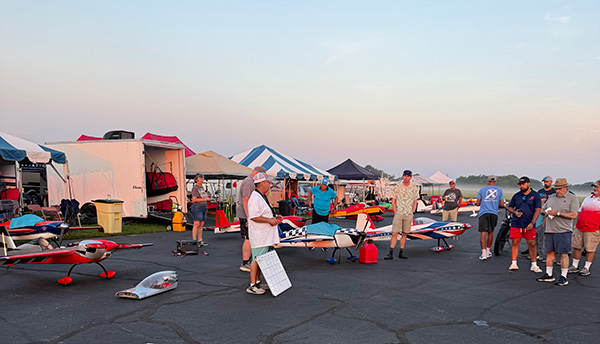 Outdoor festival with people, colorful tents, and small aircraft at dusk.