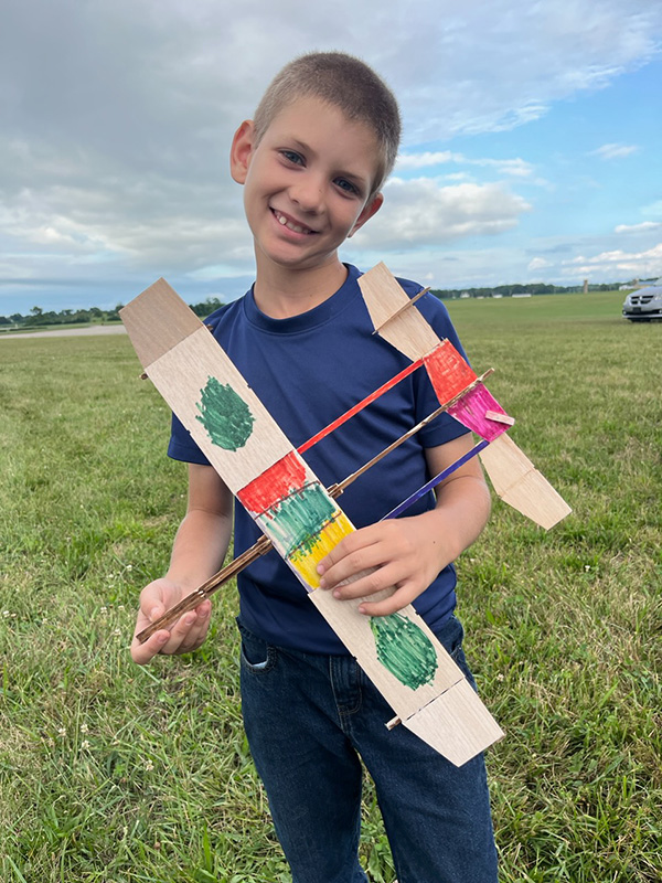 Smiling child holding a colorful toy plane on a grassy field.