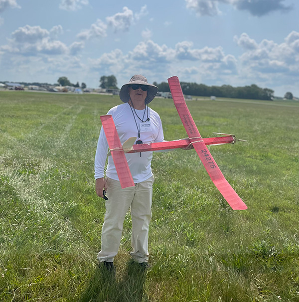Man holding a red model glider in a grassy field.