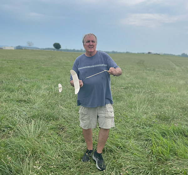 Man flying model airplane in grassy field.