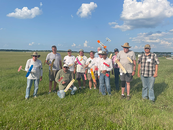 Group posing with model rockets in a grassy field under a blue sky with clouds.