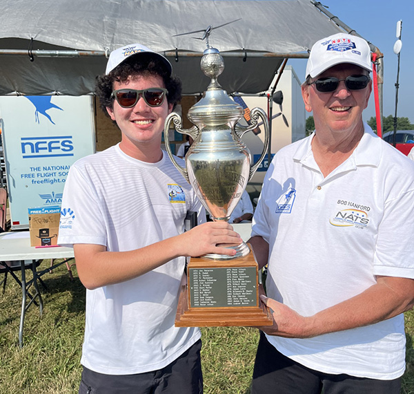 Two people in white shirts and hats holding a large trophy outdoors.