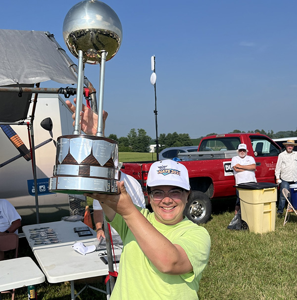 Man in a lime green shirt holding a shiny trophy outdoors with a red truck nearby.