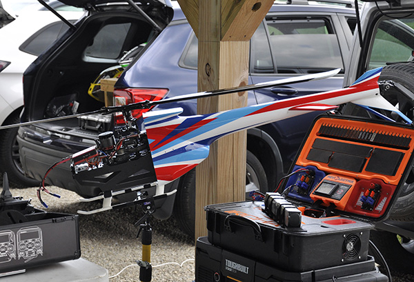 Remote-controlled helicopter with blue, red, and white tail next to equipment cases.