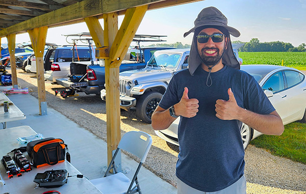 Man in outdoor setting giving thumbs up, wearing a sun hat and sunglasses.