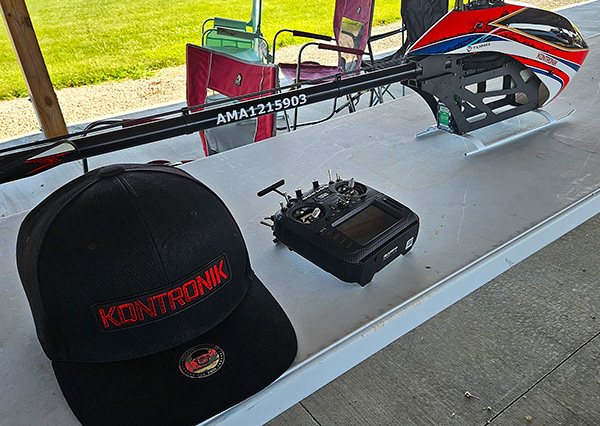 Remote control helicopter, hat, and controller on a table outdoors.
