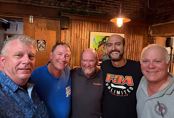 Five men smiling indoors in a warmly lit room.