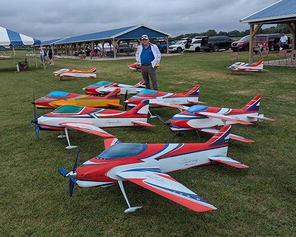 Colorful model planes on grass with a man in the background.