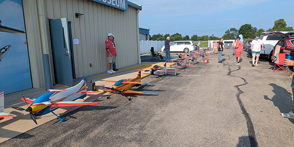 Toy airplanes lined up on a tarmac with people walking nearby.