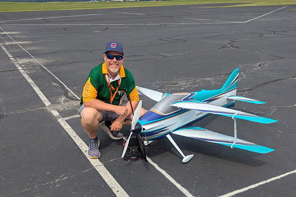 Man kneeling next to large model airplane on asphalt.