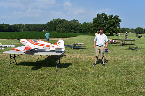 Man standing in a field beside a table with model airplanes.