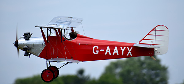Red vintage biplane in flight with clear sky backdrop.