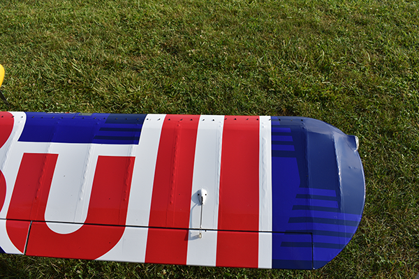 Airplane wing with bold red, white, and blue design on grassy field.