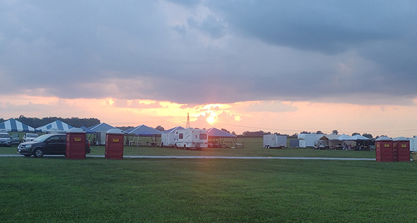 Sunset over a grassy field with scattered tents and trailers.