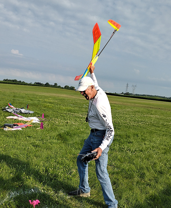 Man launching a colorful model airplane in a grassy field.