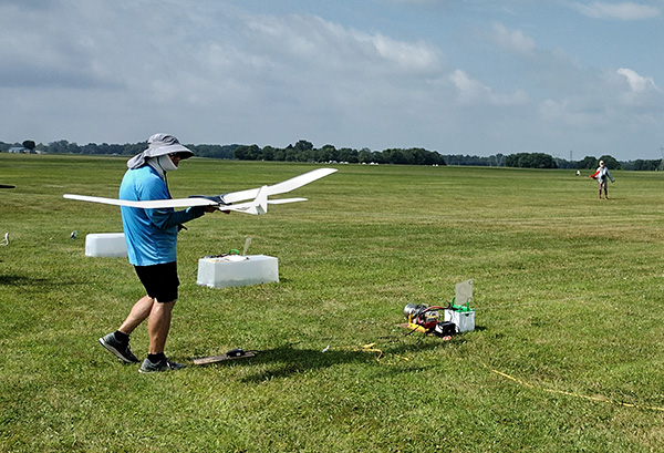 Person holding a small white aircraft on a grassy field under a cloudy sky.