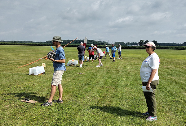 People flying model rockets on a grassy field under a cloudy sky.