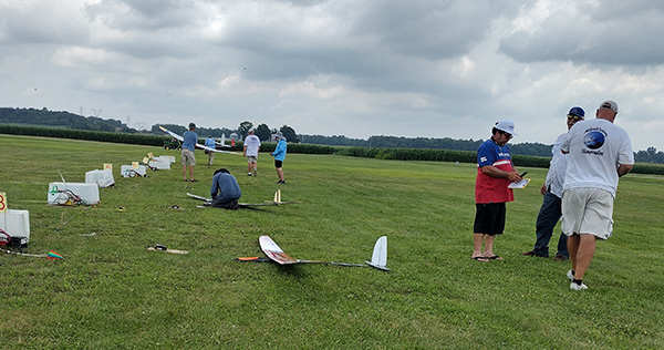 Model aircraft lined up on a grassy field with people preparing them.