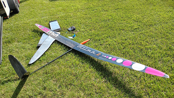 Model glider with colorful wings on grass, remote nearby.