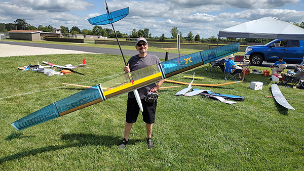 Man holding large blue and yellow model aircraft at park event.