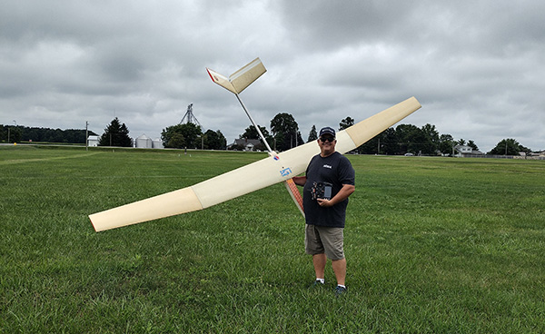 Man holding remote control beside large model airplane on grass field.