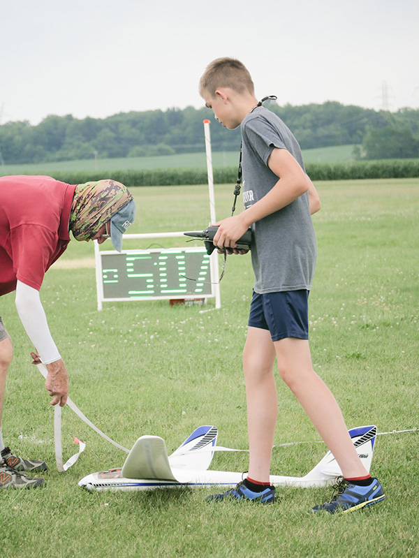 Two people preparing model aircraft for launch on grassy field.