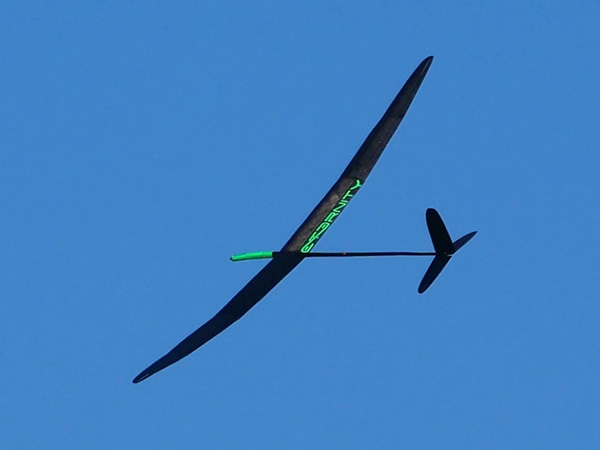 A sleek, black glider with a green detail against a clear blue sky.
