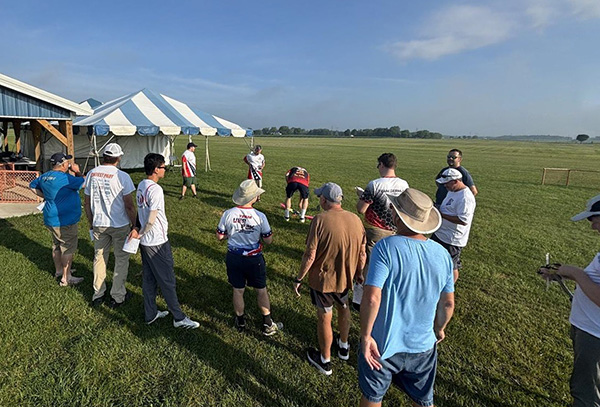 People gathered on a grassy field near a tent under a clear blue sky.