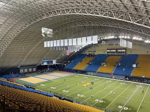 2025 Indoor FF Introduction Indoor football stadium with players on the field and rows of blue and yellow seats.