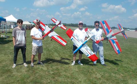 Four people holding large colorful model airplanes outdoors.