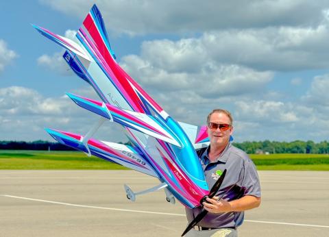 Man holding colorful model airplane on an airstrip under a partly cloudy sky.