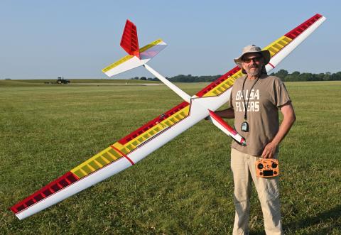 Man holding large model glider on grass field, wearing a sun hat and sunglasses.