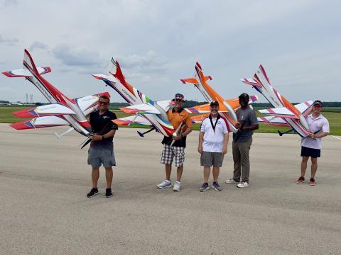 Five people holding colorful model airplanes on an airfield runway.