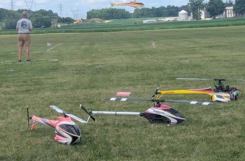 Remote-controlled helicopters on grass, with operator nearby.