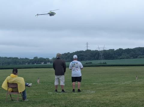 Remote-controlled helicopter flying over a field with three people watching.