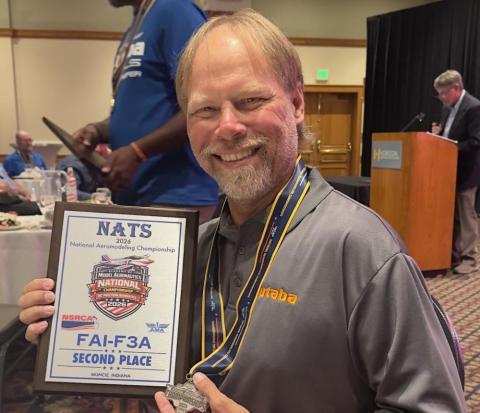 Man smiling with plaque and medal at an indoor event.