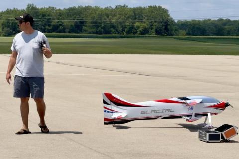 Man with remote near large model airplane on tarmac.